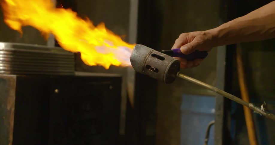 A man in a shop lights a torch and holds it next to metal cabinet