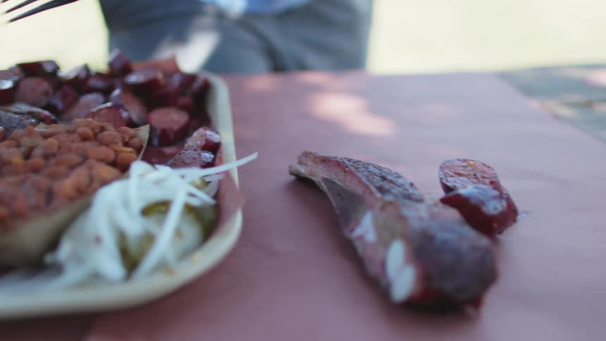Man with blue shirt and gray pants takes steak and sliced sausage in the garden