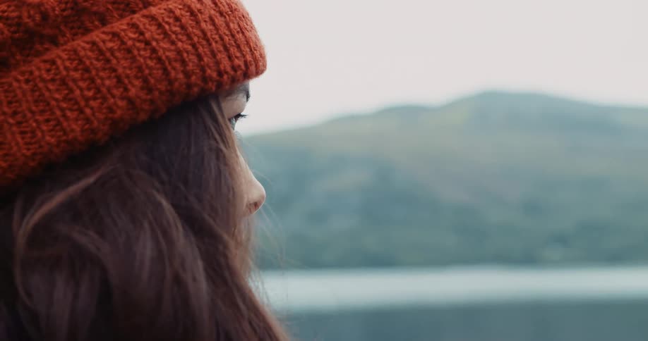 Woman with red woolly hat and hair opes her eyes and looking at lake
