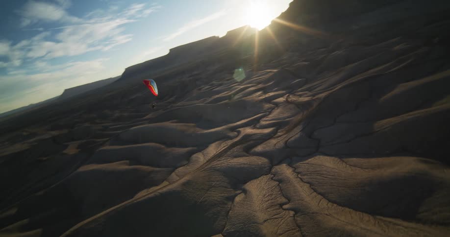 A paraglider guides their flight going up and down over sand dunes