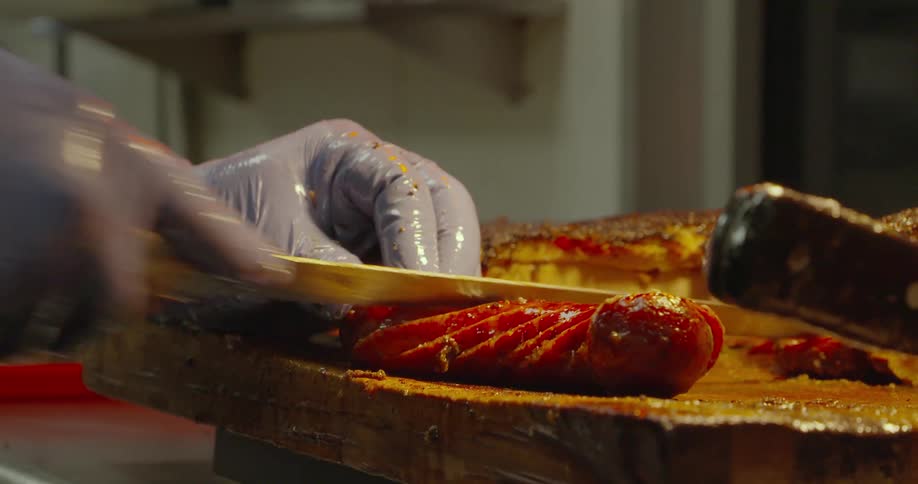 A chef slices a sausage on a cutting board inside a restaurant