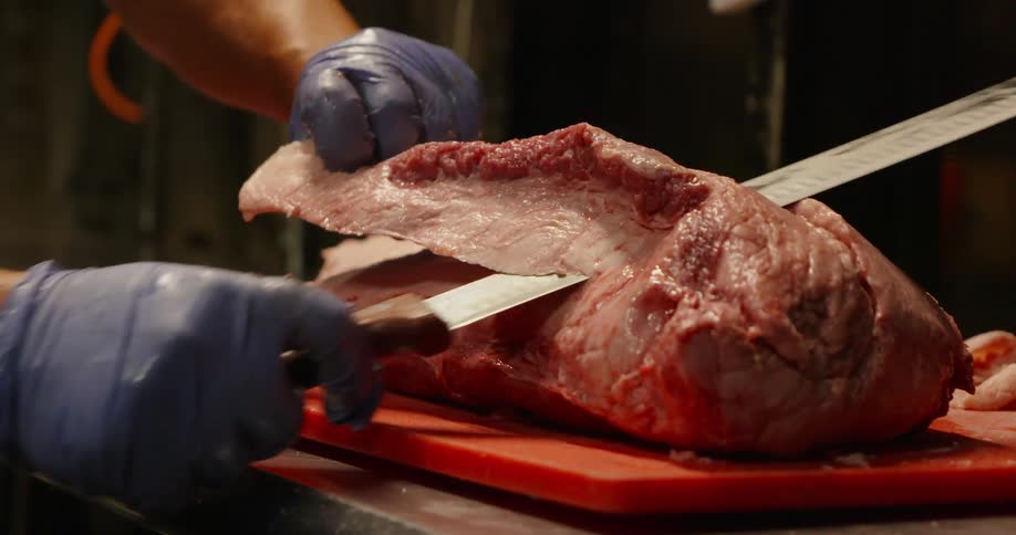 A chef trims fat off a large piece of meat