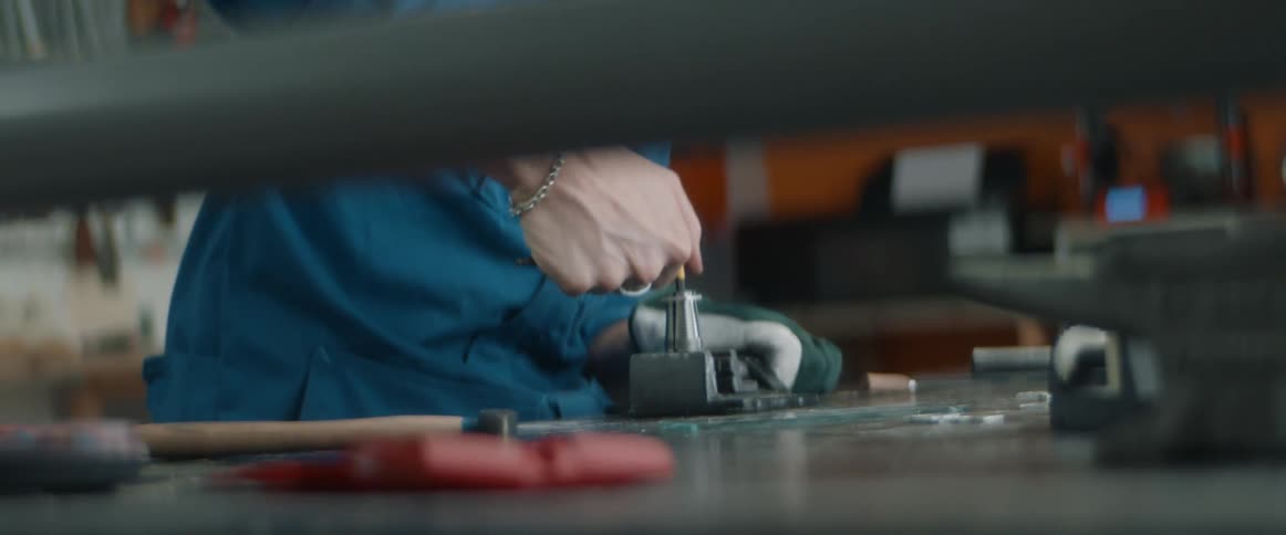A man tightens a piece of metal into a vice on top of a work bench