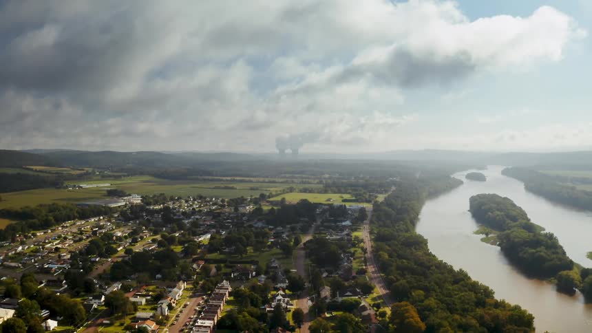 Aerial view of Susquehanna river next to town under clouds. Steam rises from a nuclear power plant in the distance.