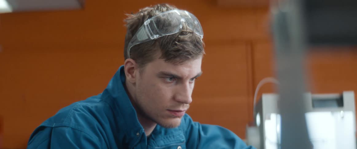 Man puts his safety glasses up so he can more easily examine part he is repairing