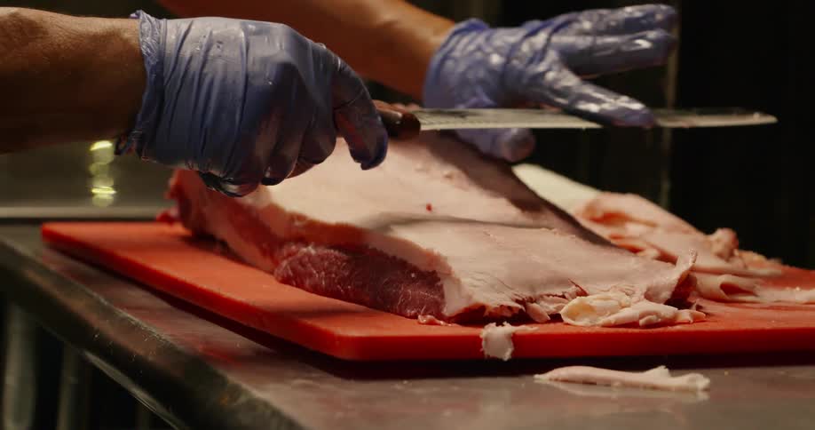 A man in a restaurant trims fat of a large cut of meat