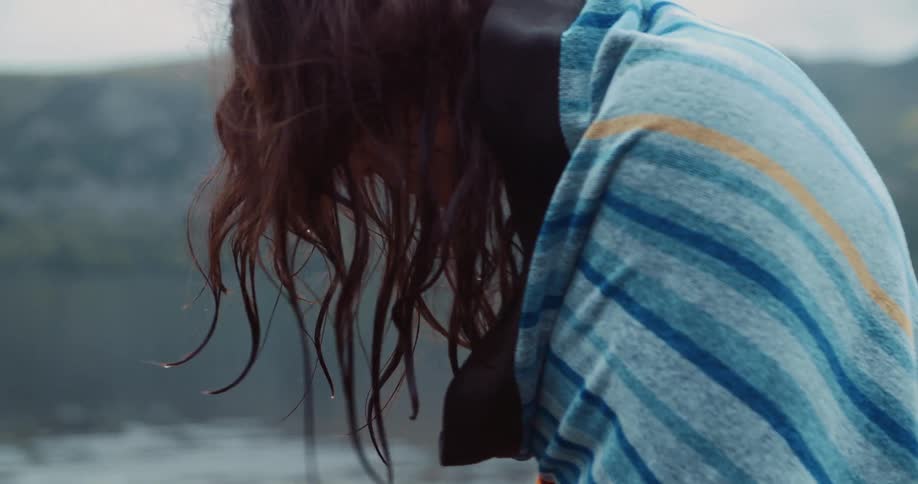 Woman with red hair and blue towel walks on lake bank on cloudy day