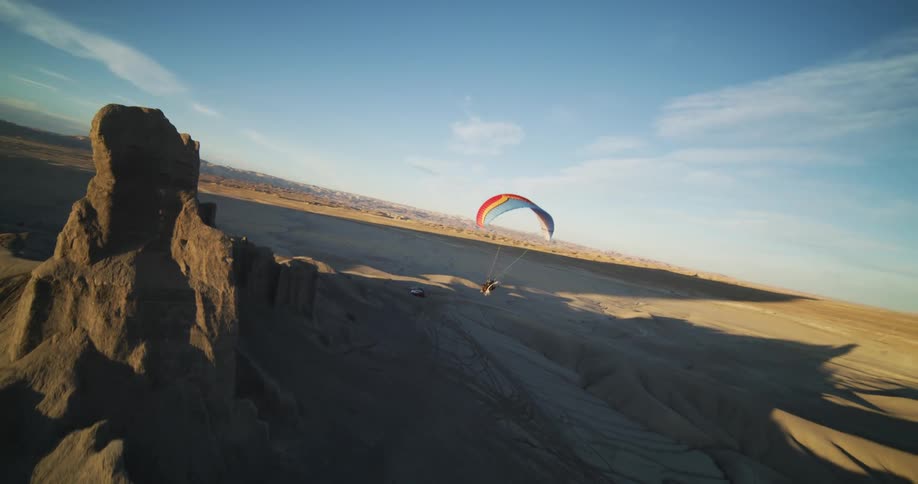 A paraglider sails high above sand dunes and canyon peaks