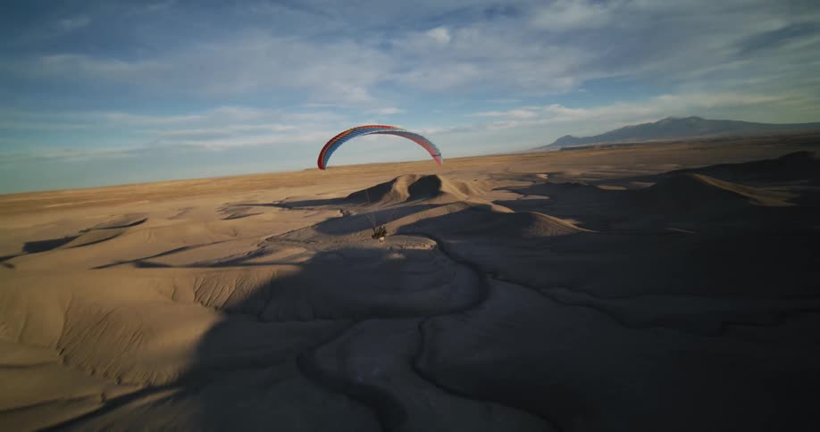 Person para sails over shadowed desert under a cloudy sky