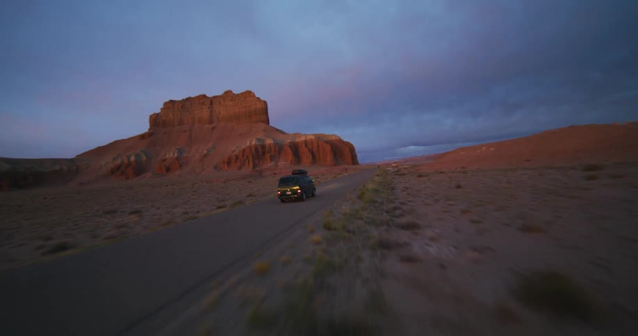 A van travels on a desert road with rock formations and mesa