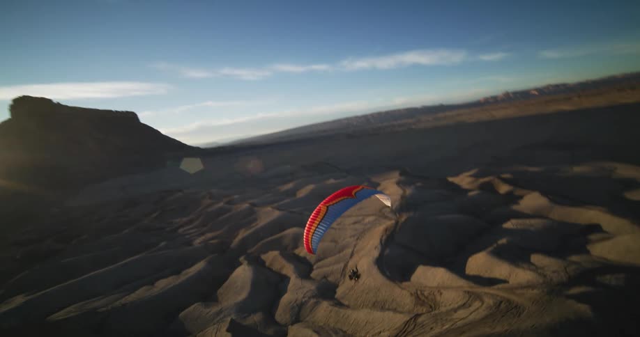 A paraglider flies up and down over dunes in the desert