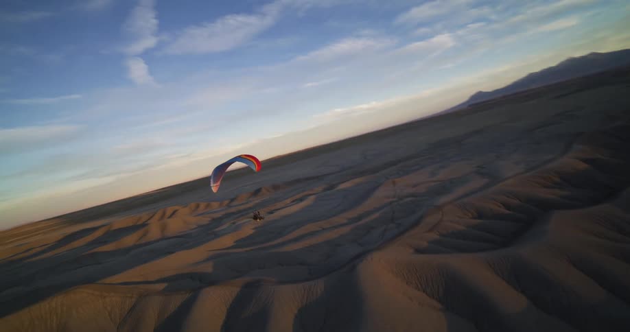 A person paraglides over a desert