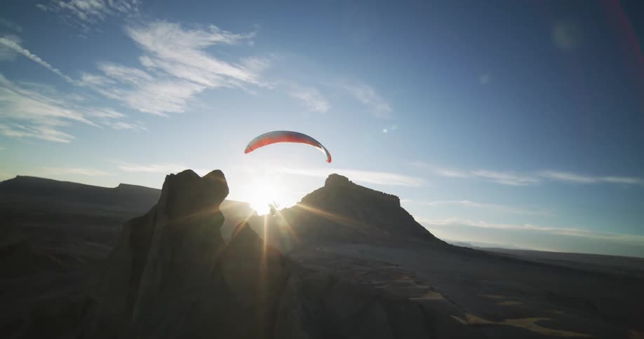 A person parachutes just above the tall sand formation in the desert