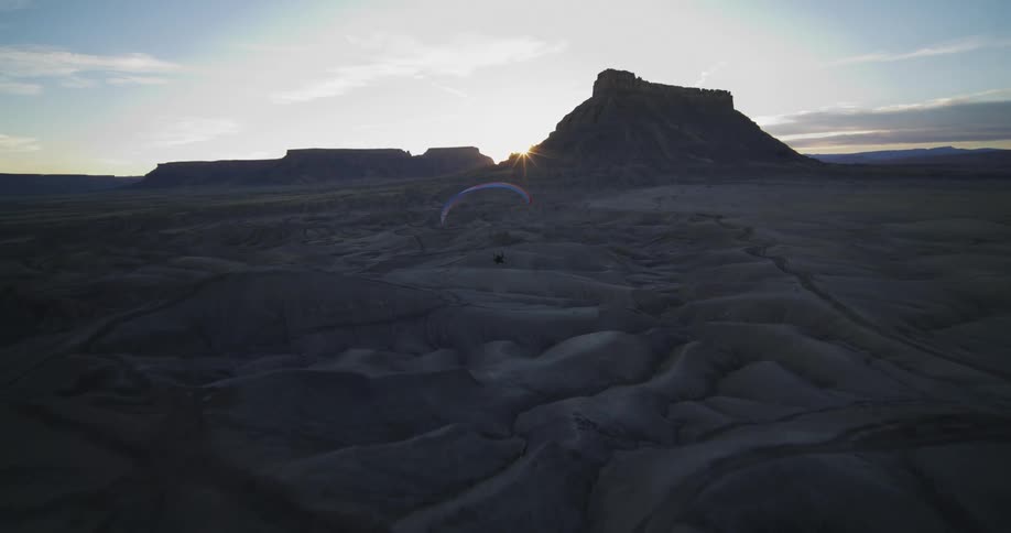 A paraglider moves closer to the ground while flying over sand dunes