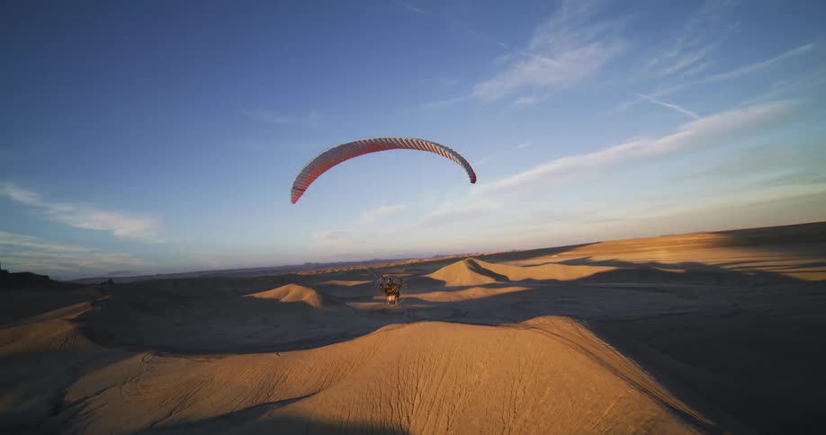 A hang glider floats over the desert dunes