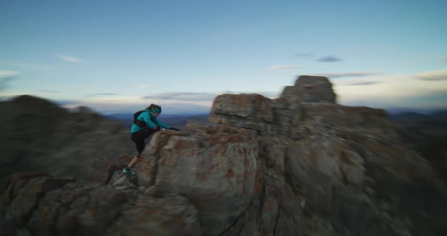 A female hiker climbs up a tall stone cliff above the canyon