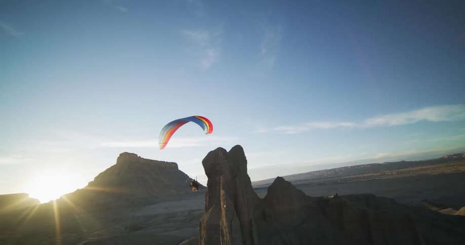 A paraglider flies over and close to a mesa in a canyon