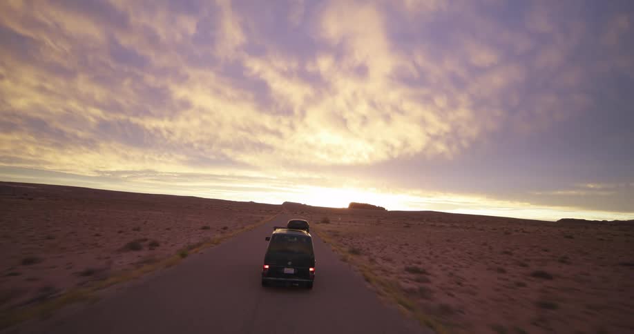 A van is traveling on a desert road under a bright cloudy sky