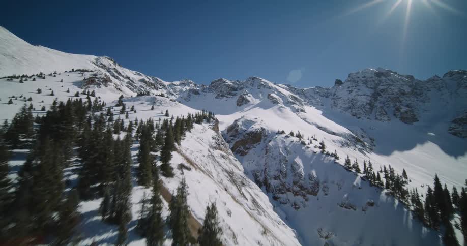 Aerial view of snowy mountain slope with forest against the clear sky