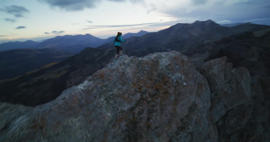 A woman running on the ledge of a cliff stops and looks down below her
