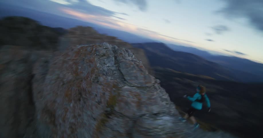 Hiker moves along ridge in mountainous country with red tinted horizon in background