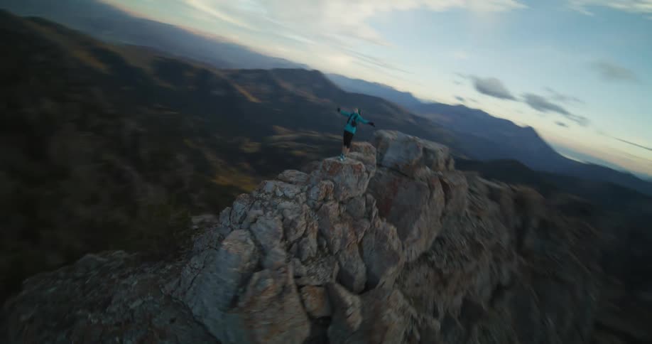 A woman wearing shorts is standing on top of a mountain ridge holding out her arms