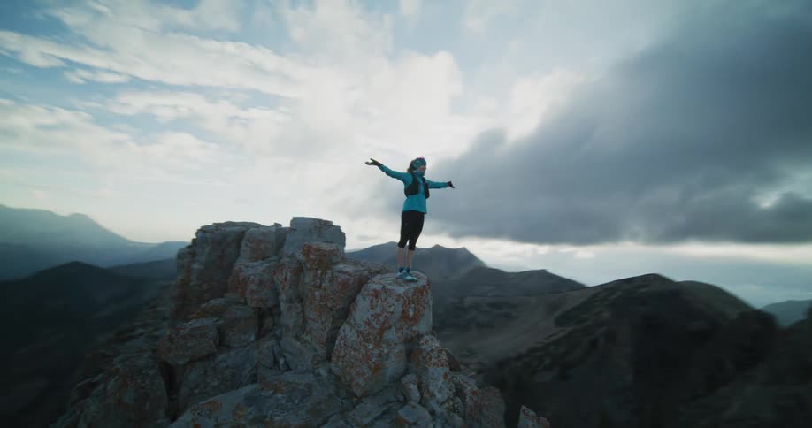 A woman throws her arms up and out after climbing to a mountain peak