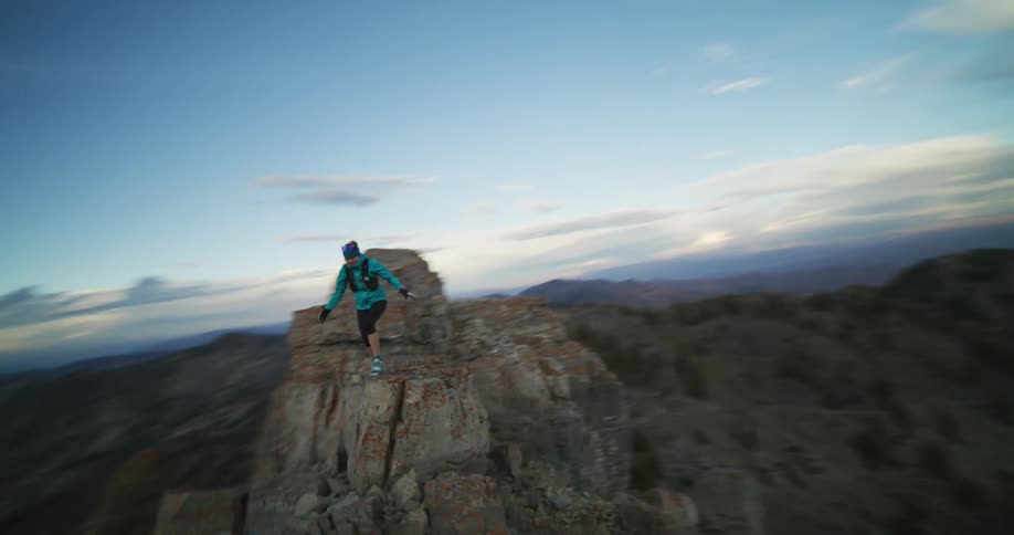A woman runs and jumps from one ledge to another on a cliff
