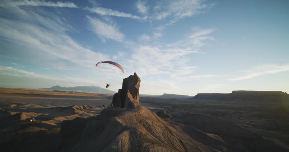 A hang glider flies over rock formations in the desert