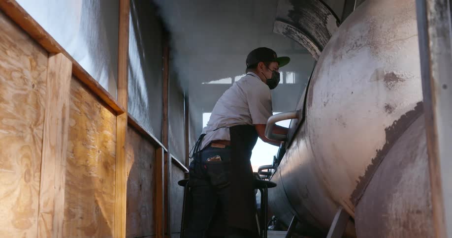 A cook removes a rack of meat from the inside of a smoker