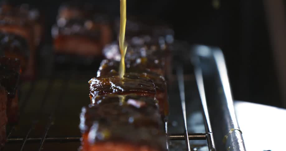 A cook pours marinade on top of meat on a grilling rack