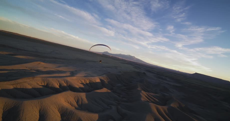 A parachute glider flies over sand dunes in a desert