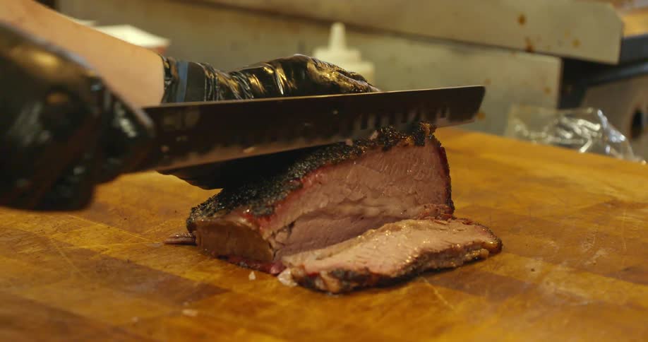 A man cuts a slab of smoked brisket into thin slices