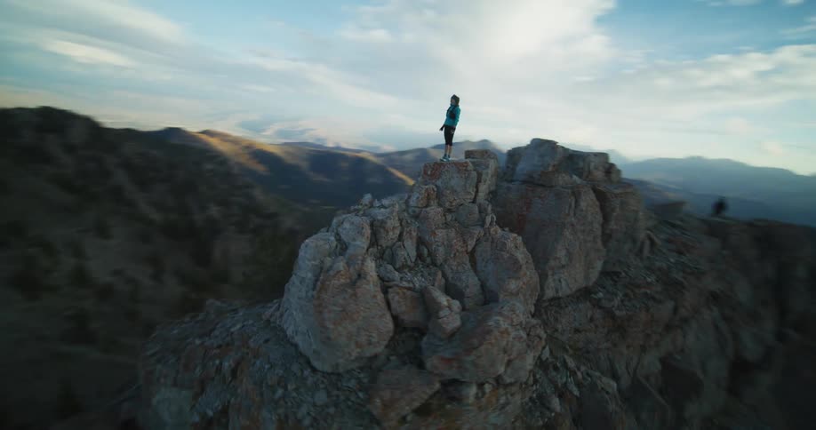 A woman wearing shorts is standing on top of a mountain ridge holding out her arms