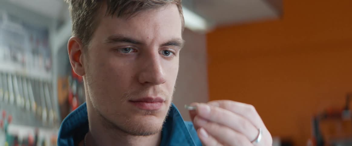A man inside a shop examines a small piece of metal