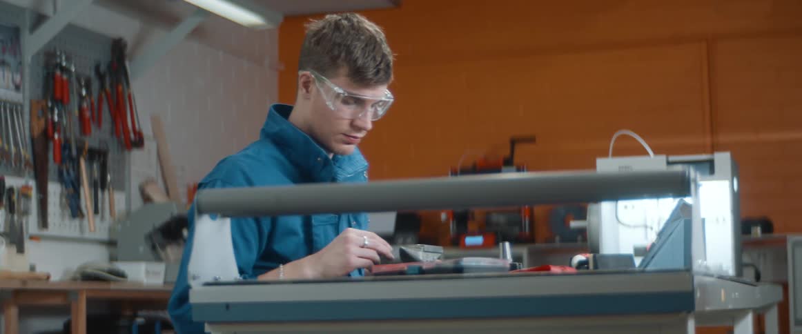 A young man sits at a work bench in a garage working on something