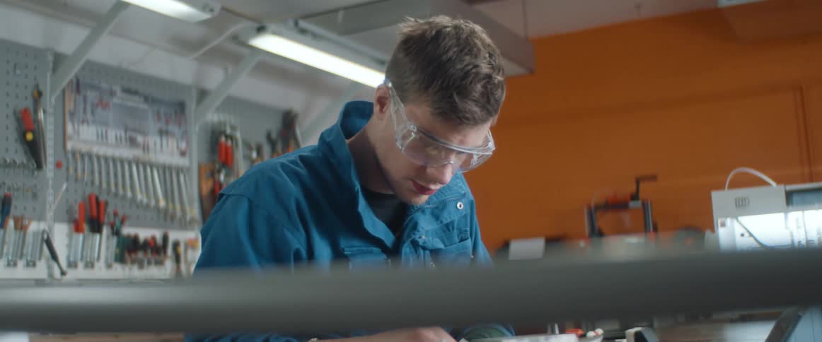 A man sits at a workbench polishing a piece of material and examining it