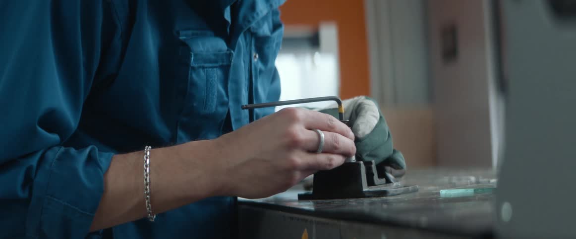 A man uses an allen wrench to tighten a tool in a workshop with a three dimensional printer
