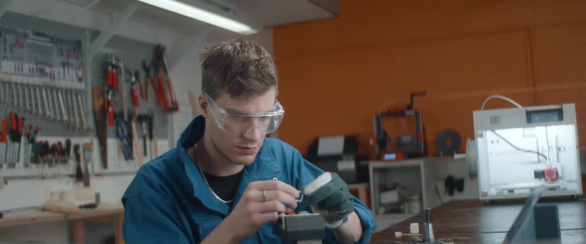 A man in a shop files a small chip and then examines it