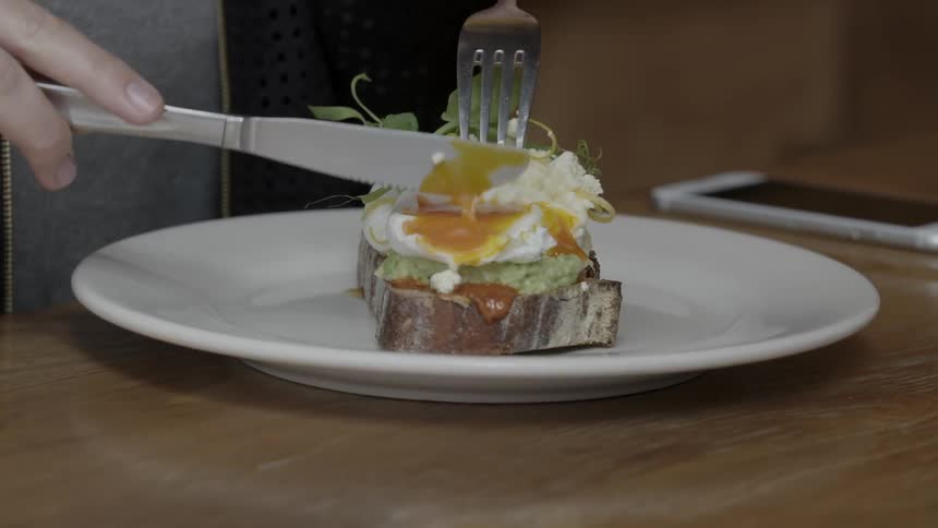 A person cuts into a poached egg on an open faced sandwich