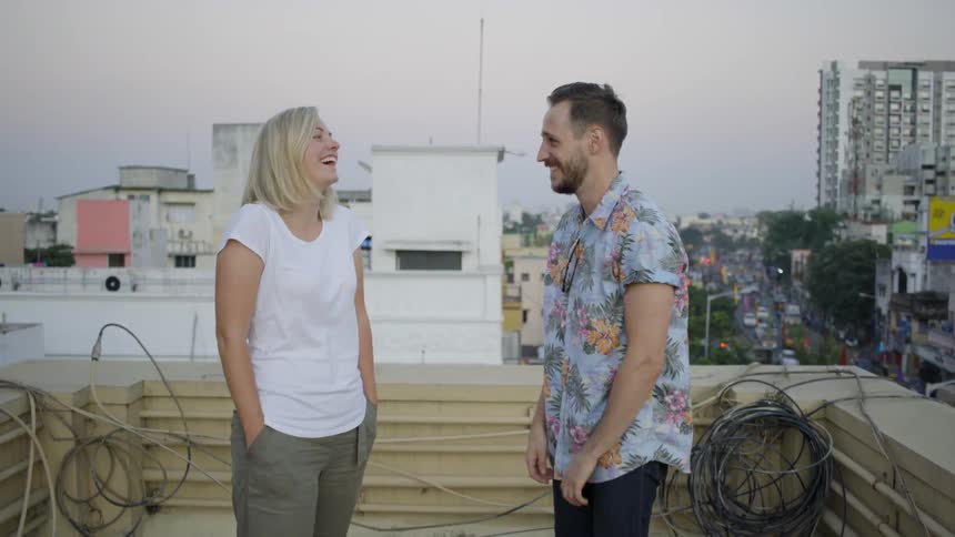Two people talk and laugh while standing on a rooftop