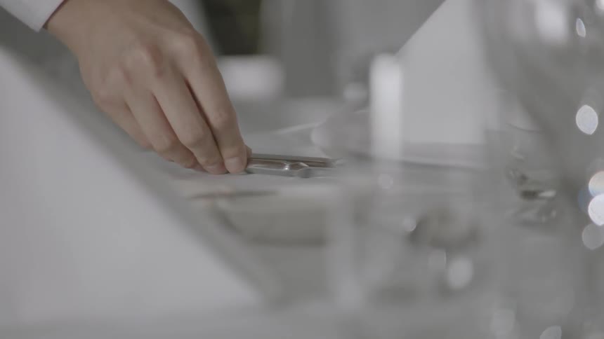 A hand positions a knife in its place in a table setting