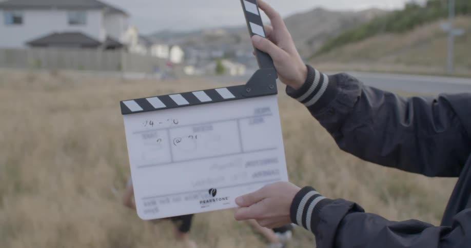 A man uses a clapperboard while two children kneel on the ground in the background