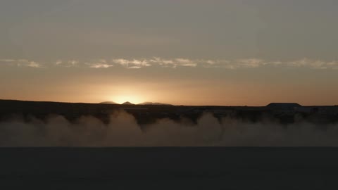 Silhouette of a race car leaving a dust trail behind on the desert at sunset