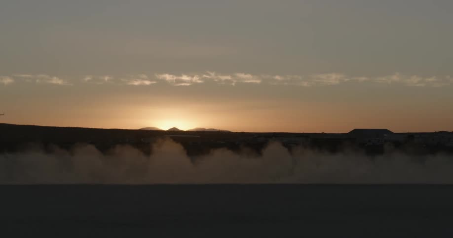 Silhouette of a race car leaving a dust trail behind on the desert at sunset