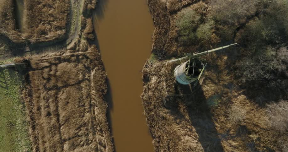 Muddy river water passes ruins and brown vegetation