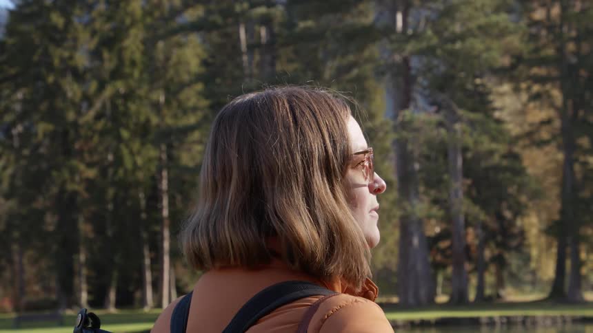 A young woman stands and looks out towards the lake and trees