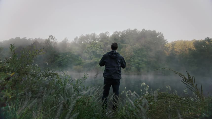Young man by river in the mist at morning
