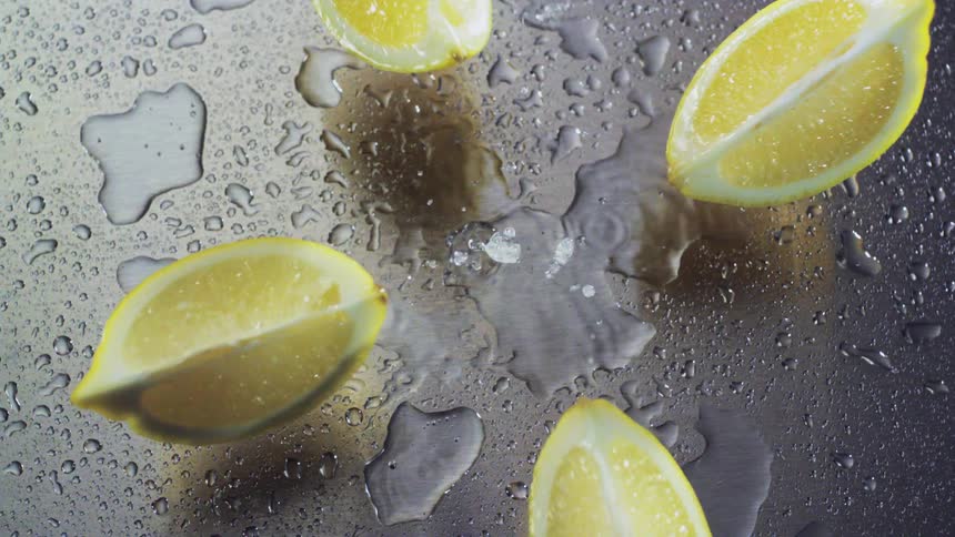 A sliced lemon falling onto a wet metal surface and breaking apart