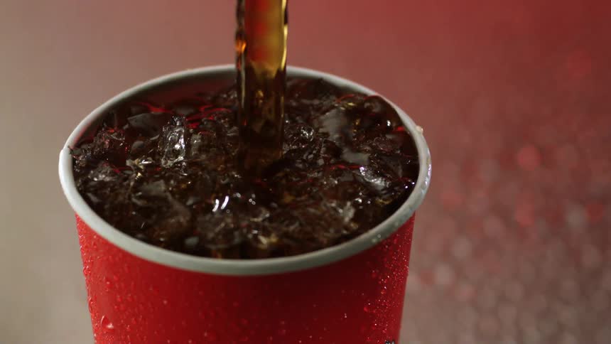Cola is being poured into a cup with ice